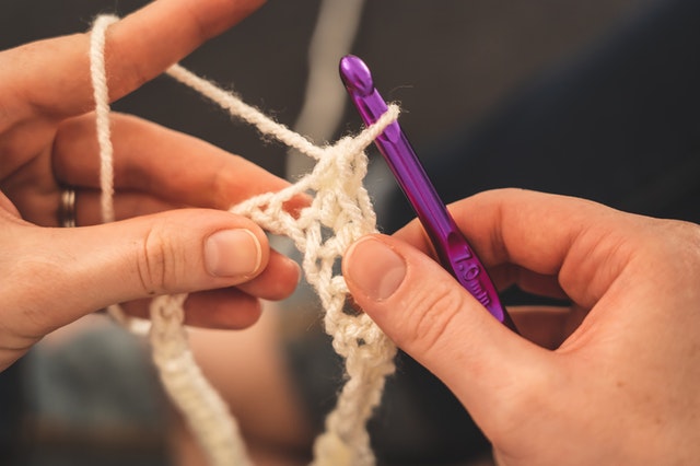 Person holding a purple crochet hook with white yarn